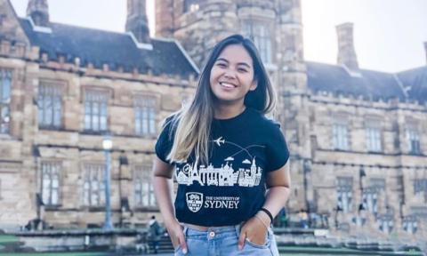 A student poses in front of a building at the University of Sydney.