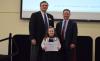 The image displays the youngest participant holding up her award to the camera 
