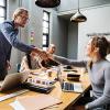 Man standing shaking woman's hand across table